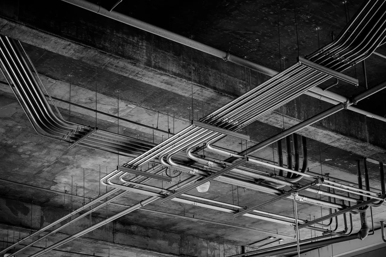 Réseau de conduits métalliques au plafond d'un bâtiment industriel en noir et blanc