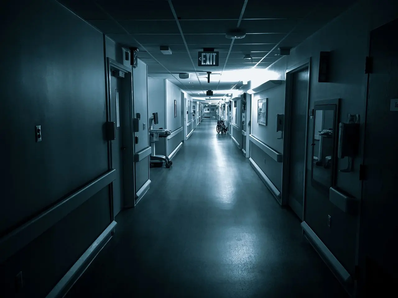 Long couloir d'hôpital sombre avec portes et lumière froide au fond